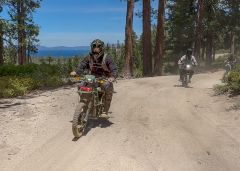 dirt bikers riding on a trail overlooking lake tahoe on a sunny day