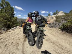 two dirt bikers kissing with their helmets on on a dirt trail with blue sky.