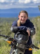 Teen age girl sitting on a dirt bike over looking blue lake with blue sky