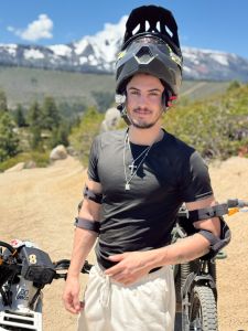 Guy standing in front of a dirt bike withe helmet half off