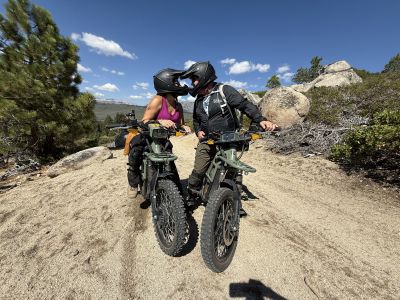 two dirt bikers kissing with their helmets on on a dirt trail with blue sky.